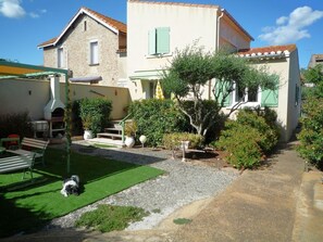 Ein zweistöckiges Haus mit einer Terrasse, einem kleinen Garten und einem Hund.