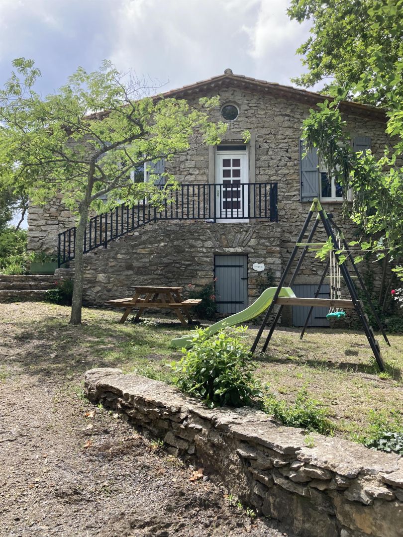 Een stenen huis met een balkon, een houten schommel en een picknicktafel.