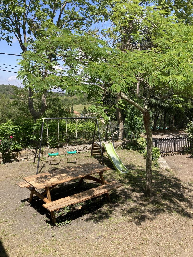 A playground with a swing set, a slide, and a picnic table in a wooded area.
