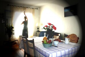 Ein Essbereich mit einem Tisch für zwei Personen, einer Blumenvase und einer Person, die am Fenster steht.