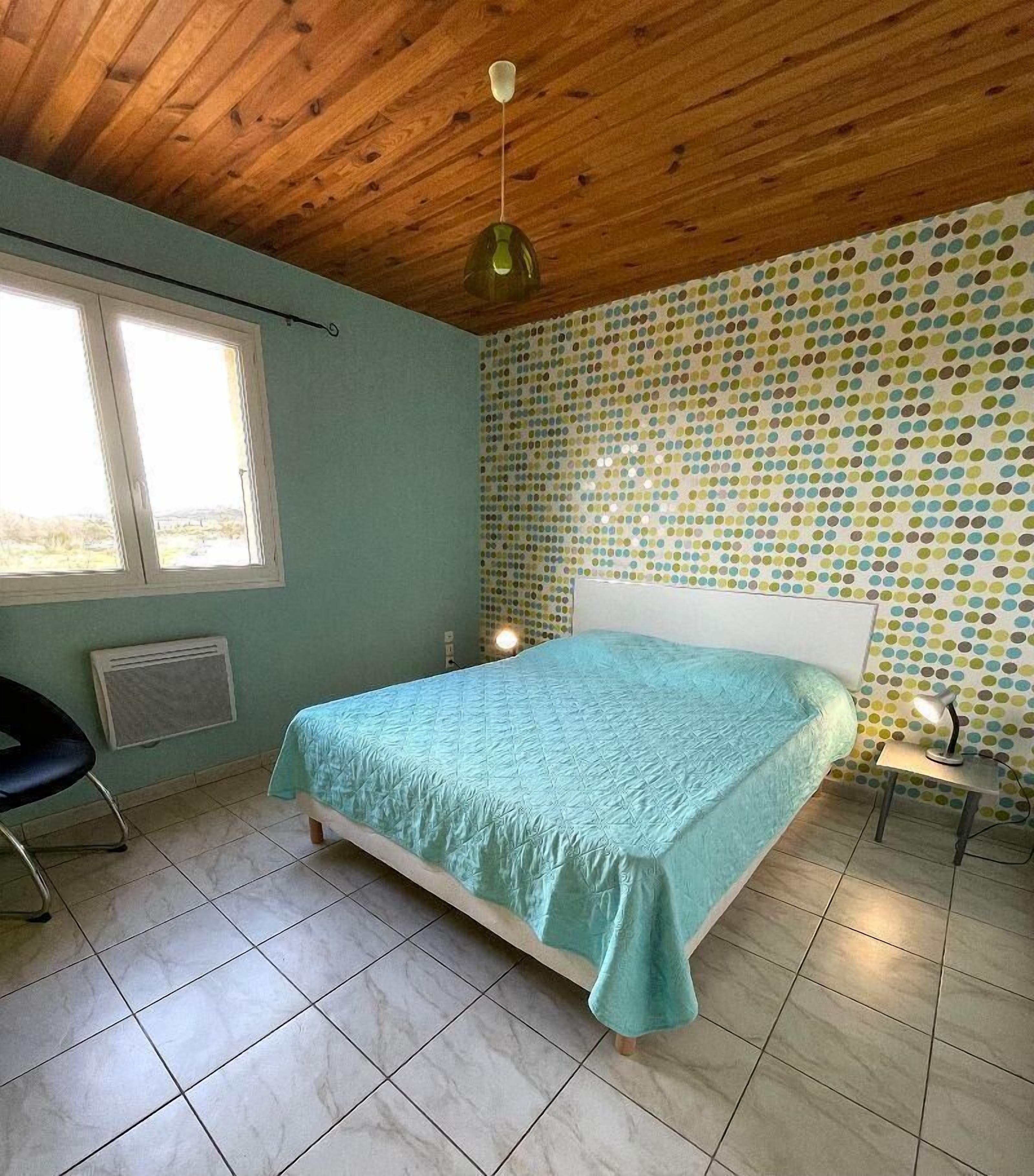 A bedroom with a bed, a chair, a radiator, a window, and a polka dot wall.