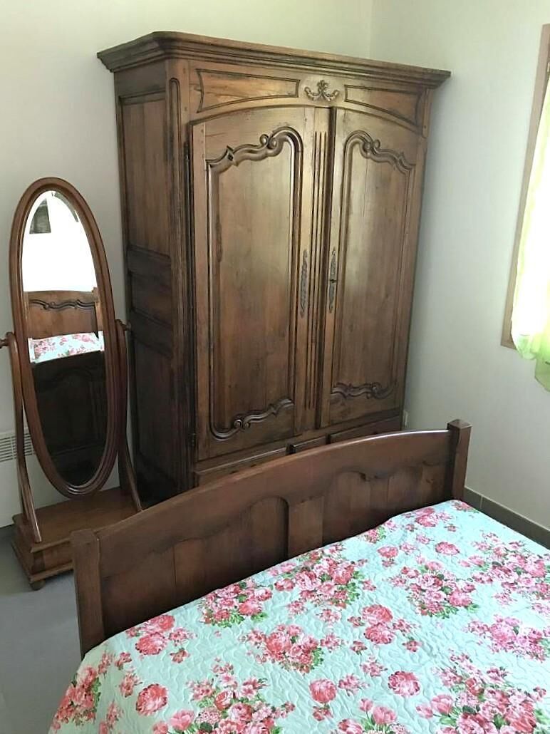 Een slaapkamer met een houten garderobe, een bed met een bloemenprint en een lange spiegel.
