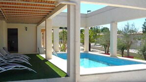 A covered outdoor area with a pool, lounge chairs, and a door leading to a building. - Les Oliviers - CARCASSONNE (CARCASSONNE)