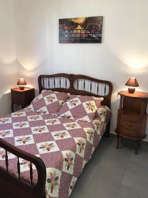 Een bed met een quilt met bloemenmotief, twee nachtkastjes met lampen, en een schilderij aan de muur.