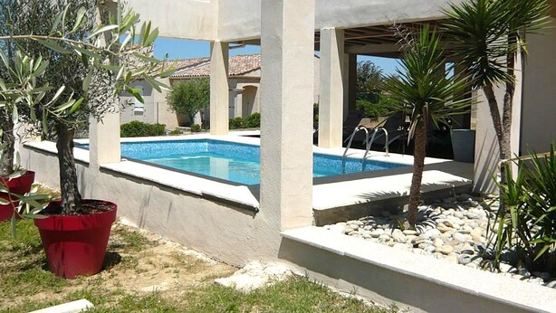 A pool area with a clear blue pool, surrounded by potted plants and a stone border. - Les Oliviers - CARCASSONNE (CARCASSONNE)