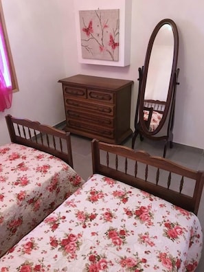Een slaapkamer met twee houten bedden, een houten dressoir, een spiegel en een schilderij aan de muur.