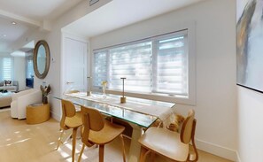 A modern dining area with a glass table, wooden chairs, and a large window with blinds. - Modern 4-Bedroom, 3-Bath Luxury Home – Newly Renovated Retreat (Toronto)