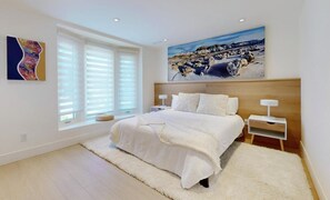 A bedroom with a large bed, white bedding, a wooden headboard, a painting above the bed, and a window with blinds. - Modern 4-Bedroom, 3-Bath Luxury Home – Newly Renovated Retreat (Toronto)