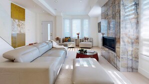 Een moderne woonkamer met een beige modulaire bank, een glazen salontafel en een flatscreen televisie bevestigd aan een marmeren muur.