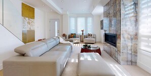 A modern living room with a beige sectional sofa, a glass coffee table, and a flat-screen TV mounted on a marble wall. - Modern 4-Bedroom, 3-Bath Luxury Home – Newly Renovated Retreat (Toronto)