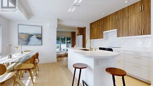 Een moderne keuken met houten kastjes, een witte aanrecht en een eethoek met een glazen tafel en stoelen.