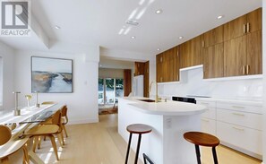 A modern kitchen with wooden cabinets, a white countertop, and a dining area with a glass table and chairs. - Modern 4-Bedroom, 3-Bath Luxury Home – Newly Renovated Retreat (Toronto)