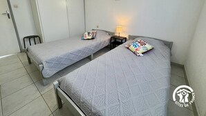 Et dobbeltværelse med to senge, hver med et mønstret sengetæppe og pude. Der er et lille bord med en lampe imellem sengene.