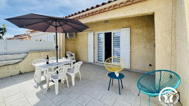 En terrasse med et bord, stole og en parasol, samt en gul stol.