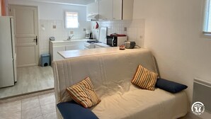 A compact living space with a kitchenette, a sofa with cushions, and a small trash bin. - Camplong l'Alaric - CAMPLONG D'AUDE (CAMPLONG D'AUDE)