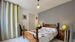 A bedroom with a wooden bed, two bedside tables with lamps, a striped curtain, and a tiled floor. - Camplong l'Alaric - CAMPLONG D'AUDE (CAMPLONG D'AUDE)