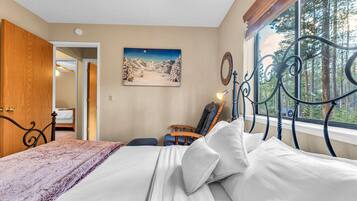 A bedroom with a bed, a wooden door, a painting, a window with a view of trees, and a metal headboard.