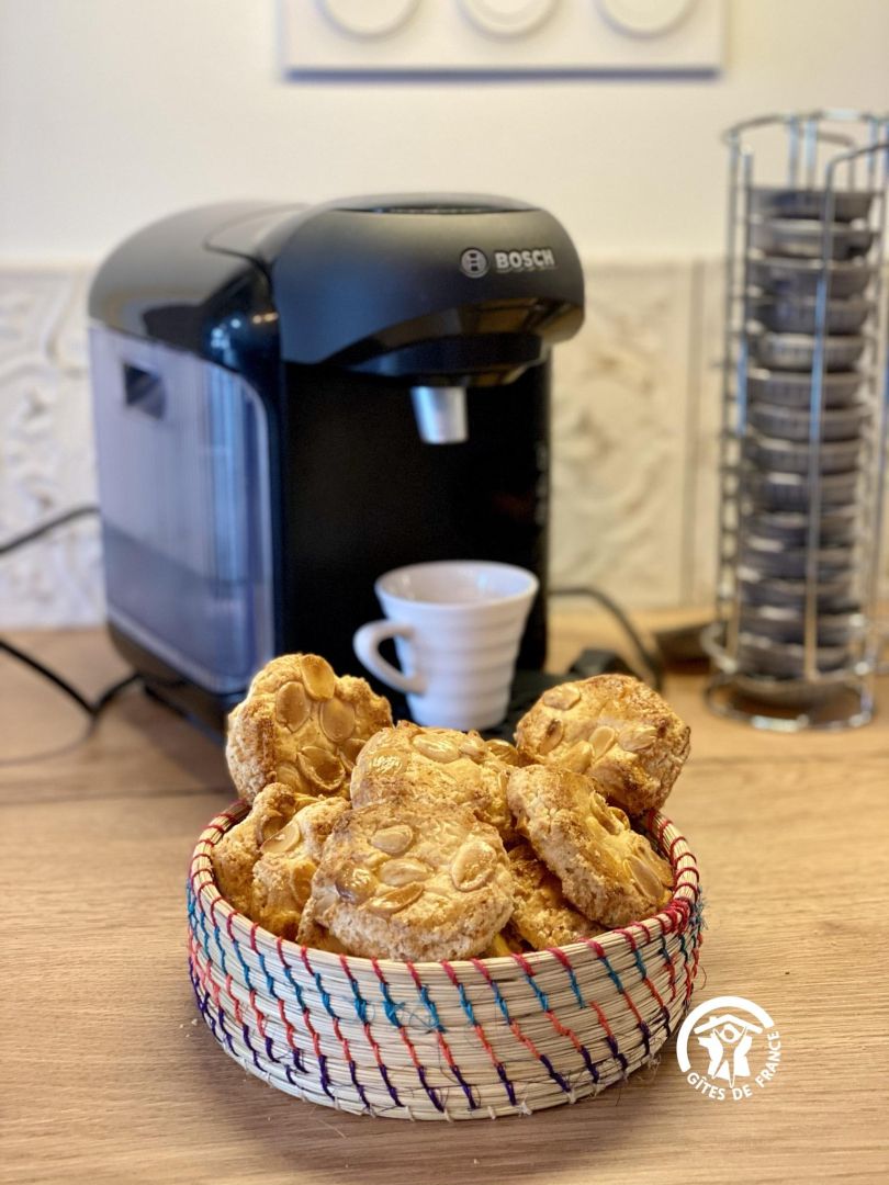 Una cafetera, una taza de café y una cesta de galletas sobre una mesa de madera.