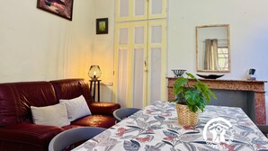 Una stanza accogliente con un divano in pelle rossa, un tavolo con tovaglia floreale, una lampada e una pianta.