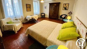 Quarto com cama grande, mesinha, duas cadeiras, guarda-roupa e janela com cortinas.