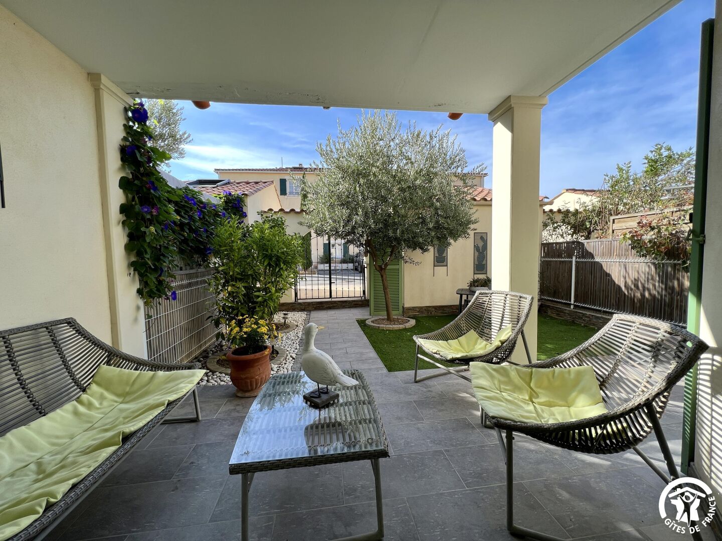 A covered patio with wicker furniture, a table, and a potted plant.