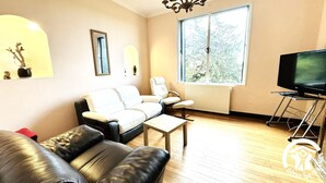 A living room with a sofa, armchair, coffee table, and a TV on a stand. - Le Clos de la Tour 2 (Carcassonne)