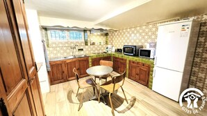 A compact kitchen with wooden cabinets, a round table, and a white refrigerator. - Le Clos de la Tour 2 (Carcassonne)