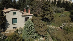 A stone building with a small window and a door, surrounded by trees and a castle in the background. - Le Clos de la Tour 2 (Carcassonne)