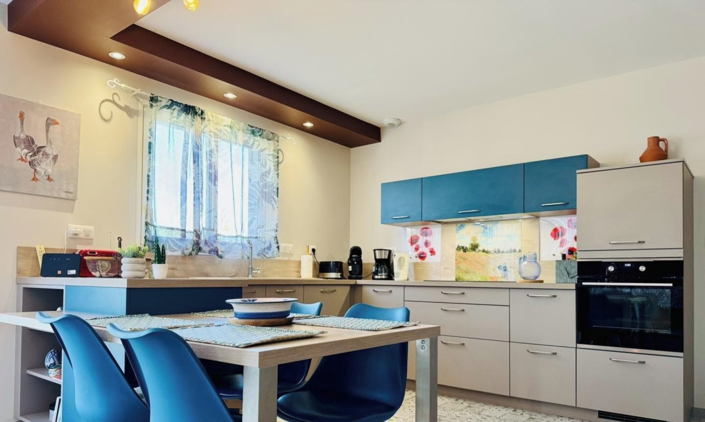 A modern kitchen with a dining area, featuring a table with chairs, a coffee machine, and a refrigerator.