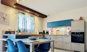 A modern kitchen with a dining area, featuring a table with chairs, a coffee machine, and a refrigerator.