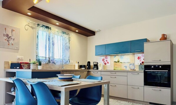 Een moderne keuken met een eethoek, met een tafel en stoelen, een koffieapparaat en een koelkast.