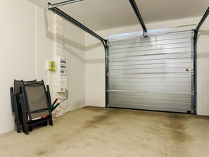A garage with a closed metal door, a power outlet box, and a chair. - Les Coquelicots - SONNAC SUR L'HERS (SONNAC SUR L'HERS)
