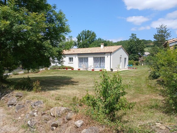 A single-story house with a tiled roof, a front porch with a table and chairs, and a small garden area with rocks and plants. - Les Coquelicots - SONNAC SUR L'HERS (SONNAC SUR L'HERS)