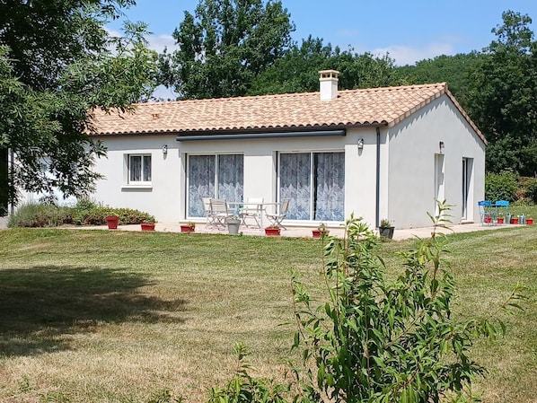 Une maison de plain-pied avec un toit en tuiles, un patio avec des meubles d’extérieur et un jardin.