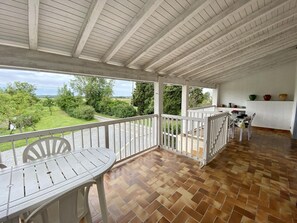 A covered patio with a wooden floor, white furniture, and a view of a green landscape. - Le Miraillou - RICAUD (RICAUD)