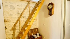 Una escalera de madera que conduce a un ático con pared de piedra, un cofre de madera y un reloj de pared.