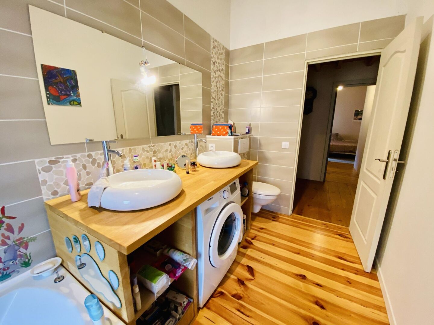 Une salle de bain moderne avec un grand miroir, deux lavabos, un lave-linge et des toilettes.