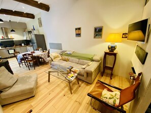 A living room with a sofa, armchair, coffee table, and a TV. There is a kitchen in the background. - Terre et Mer - ROQUEFORT DES CORBIERES (ROQUEFORT DES CORBIERES)