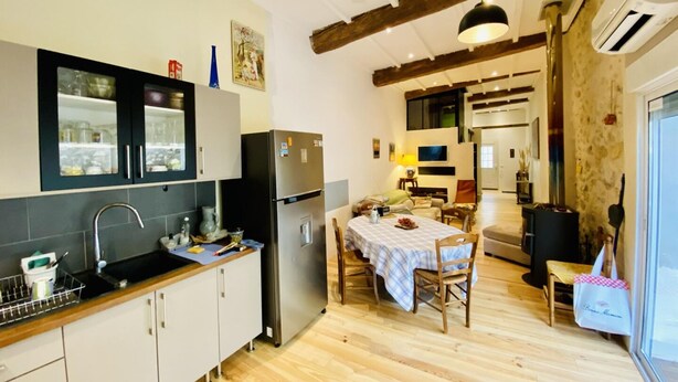 Una cocina con suelo de madera, una zona de comedor con mesa y sillas, y un ventanal grande.