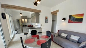 Eine moderne Küche mit grauen Schränken, einem Edelstahlkühlschrank und einem Essbereich mit rundem Tisch und schwarzen Stühlen.