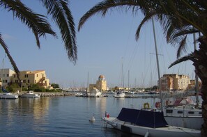 A marina with boats docked, a building with a dome, and palm trees.