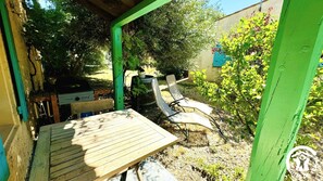 A wooden table and chairs under a green structure, with a barbecue grill and a tree in the background. - Le Mas des Oliviers - AZILLE (AZILLE)