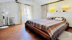 A bedroom with a wooden bed, a standing fan, a radiator, and a window with curtains. - Le Mas des Oliviers - AZILLE (AZILLE)