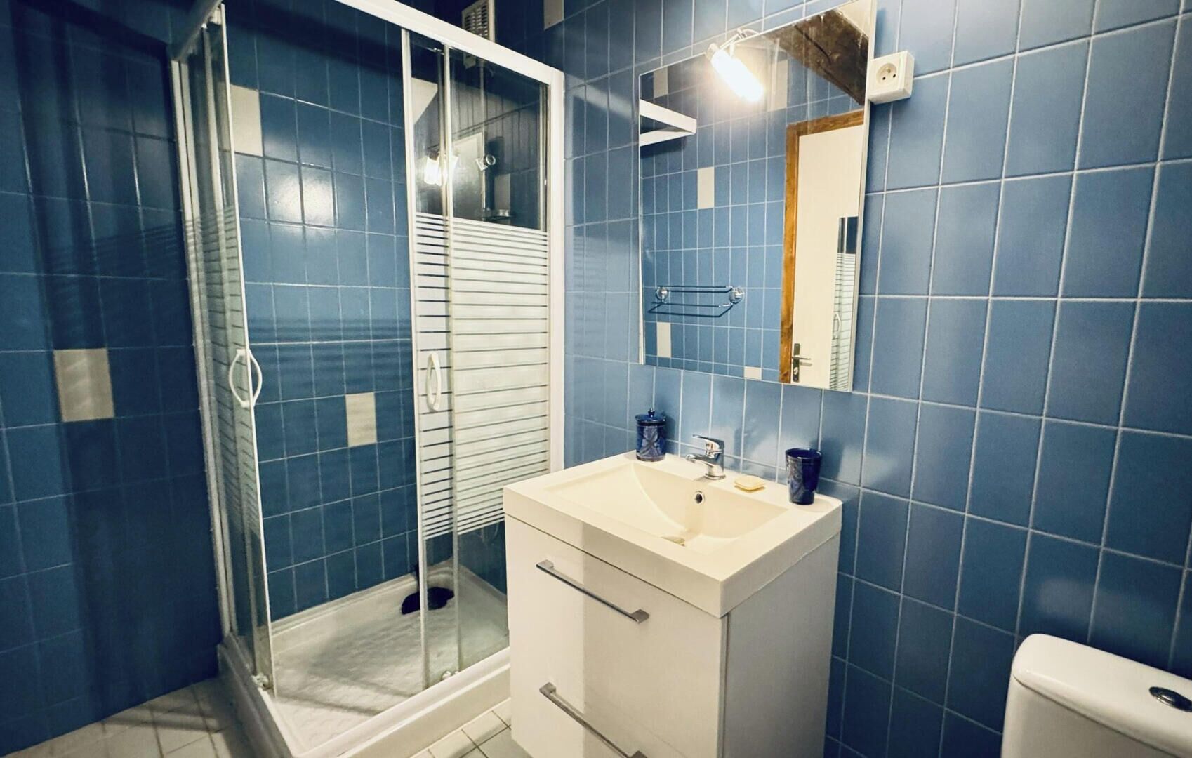 Ein Badezimmer mit blauen Fliesen, einem weißen Waschbecken, einem Spiegel und einer Duschkabine aus Glas.