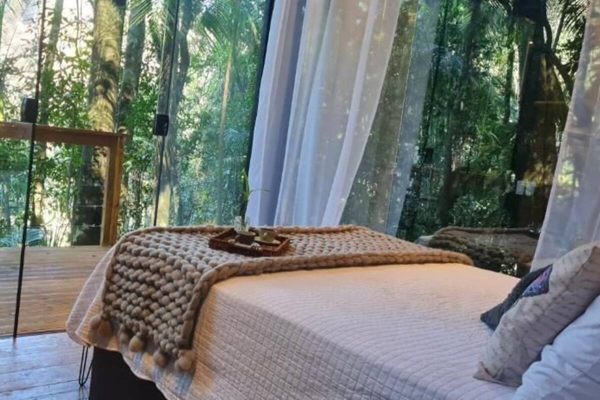 A bedroom with a bed, a wooden floor, a window with curtains, and a view of trees.