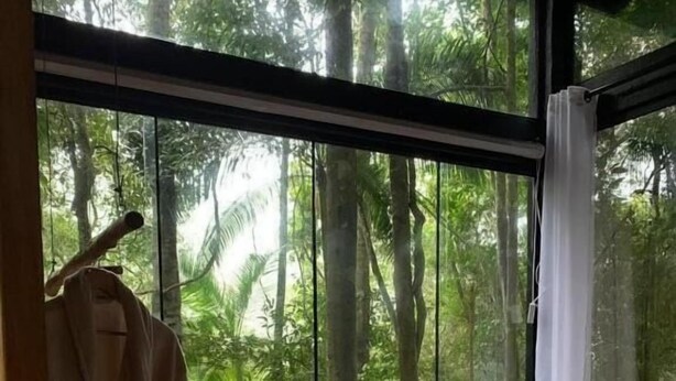 A bedroom with a large window, a wooden floor, a bed, and a hanging robe. - Tree House (Marechal Floriano)