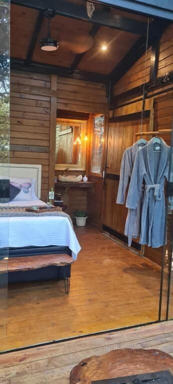 A wooden cabin interior with a bed, a mirror, and a robe rack. - Tree House (Marechal Floriano)