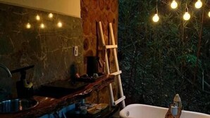 A bathroom with a bathtub, a wooden floor, a stone wall, and a hanging light fixture. - Tree House (Marechal Floriano)