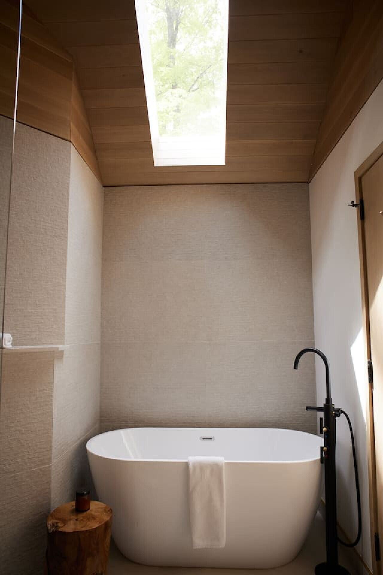 A modern bathroom with a freestanding bathtub, a wooden stool, and a skylight.
