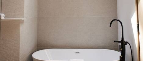 A modern bathroom with a freestanding bathtub, a wooden stool, and a skylight.
